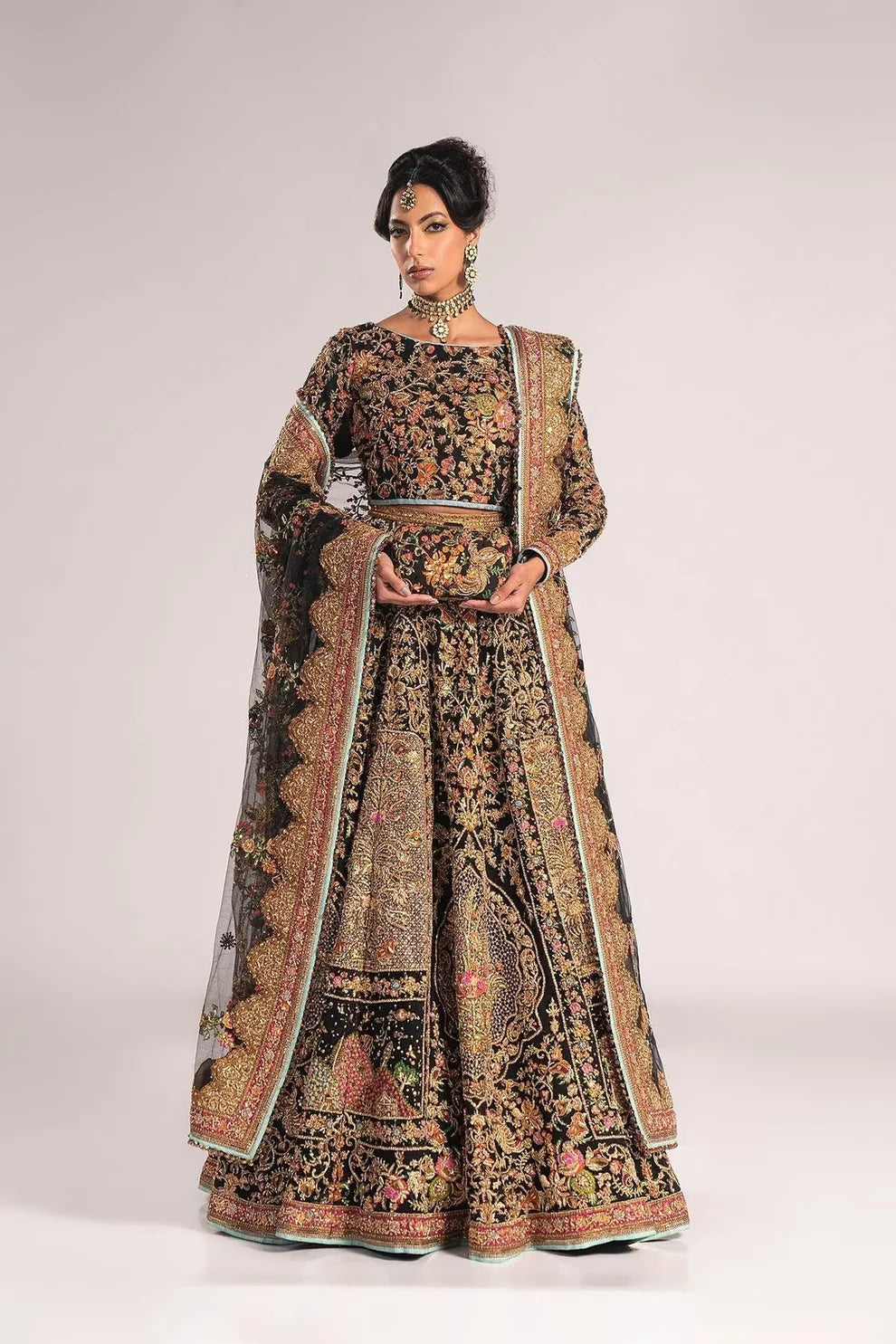 Ajooba by Fahad Hussayn luxury black bridal couture outfit front view featuring heavily hand-embellished net lehenga and blouse with intricate resham, zardozi, naqshi, dabka and crystal embroidery forming rich floral Mughal inspired patterns, dramatic structured silhouette with full flare lehenga and detailed choli, paired with sheer organza dupatta scattered with delicate floral motifs and ornate embroidered border finishing, premium high-end bridal ensemble perfect for weddings, receptions etc