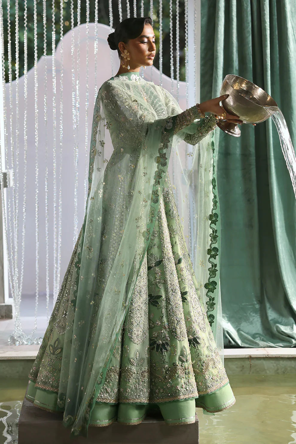 Lirien by Soraya luxury mint green couture pishwas outfit front view featuring heavily hand-embellished organza panels with intricate floral embroidery, resham threadwork, sequins, cutdana and tilla detailing arranged in elegant flowing pattern across flare, velvet accent neckline patch adding rich contrast, full embroidered sleeves and back panels, paired with lightweight net dupatta featuring embroidered sprays and delicate border finishing, along with dyed silk trouser, premium Pakistani designer outfit 