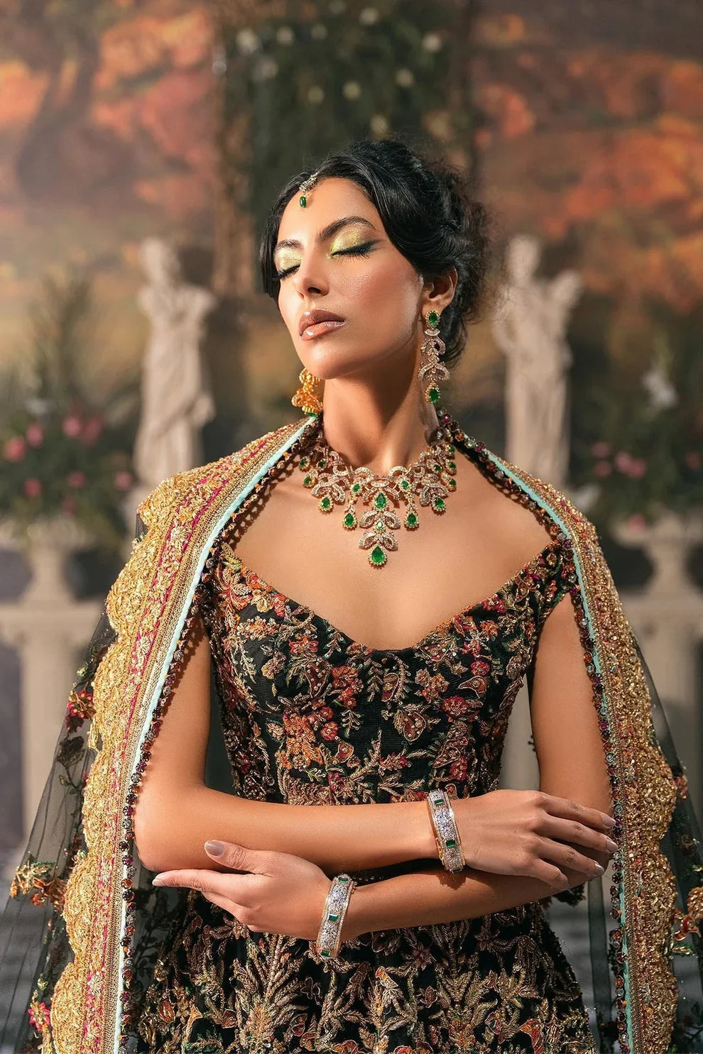 Ajooba by Fahad Hussayn luxury black bridal couture outfit front view featuring heavily hand-embellished net lehenga and blouse with intricate resham, zardozi, naqshi, dabka and crystal embroidery forming rich floral Mughal inspired patterns, dramatic structured silhouette with full flare lehenga and detailed choli, paired with sheer organza dupatta scattered with delicate floral motifs and ornate embroidered border finishing, premium high-end bridal ensemble perfect for weddings, receptions etc