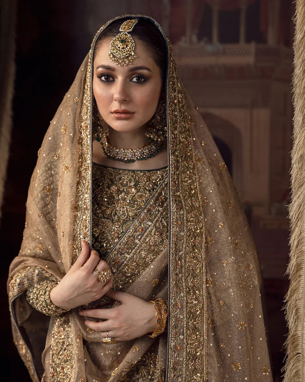 Faiza Saqlain Muntaha luxury bridal couture outfit front view featuring heavily hand-embellished raw silk shirt with intricate resham, dabka, naqshi and sequin embroidery in Mughal inspired floral motifs, paired with voluminous lehenga adorned with multiple richly embroidered borders and antique finishing, completed with a gracefully draped zari net dupatta with detailed adda work and ornate edging, premium bridal ensemble perfect for weddings, nikkah ceremonies and luxury festive occasions