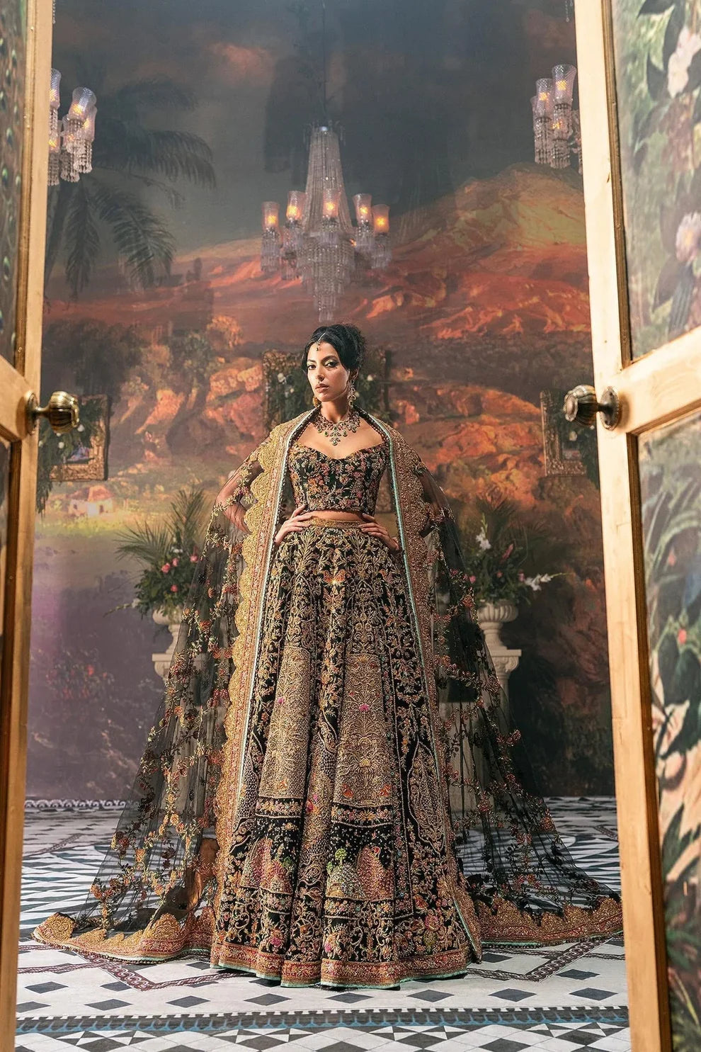 Ajooba by Fahad Hussayn luxury black bridal couture outfit front view featuring heavily hand-embellished net lehenga and blouse with intricate resham, zardozi, naqshi, dabka and crystal embroidery forming rich floral Mughal inspired patterns, dramatic structured silhouette with full flare lehenga and detailed choli, paired with sheer organza dupatta scattered with delicate floral motifs and ornate embroidered border finishing, premium high-end bridal ensemble perfect for weddings, receptions etc