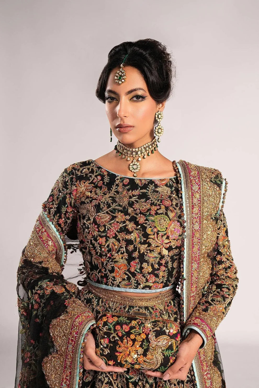 Ajooba by Fahad Hussayn luxury black bridal couture outfit front view featuring heavily hand-embellished net lehenga and blouse with intricate resham, zardozi, naqshi, dabka and crystal embroidery forming rich floral Mughal inspired patterns, dramatic structured silhouette with full flare lehenga and detailed choli, paired with sheer organza dupatta scattered with delicate floral motifs and ornate embroidered border finishing, premium high-end bridal ensemble perfect for weddings, receptions etc