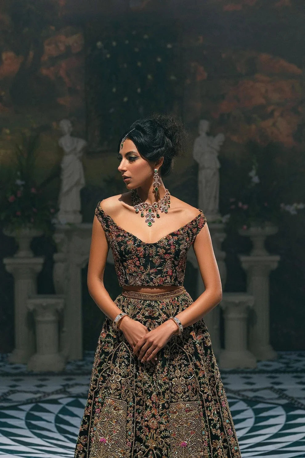 Ajooba by Fahad Hussayn luxury black bridal couture outfit front view featuring heavily hand-embellished net lehenga and blouse with intricate resham, zardozi, naqshi, dabka and crystal embroidery forming rich floral Mughal inspired patterns, dramatic structured silhouette with full flare lehenga and detailed choli, paired with sheer organza dupatta scattered with delicate floral motifs and ornate embroidered border finishing, premium high-end bridal ensemble perfect for weddings, receptions etc