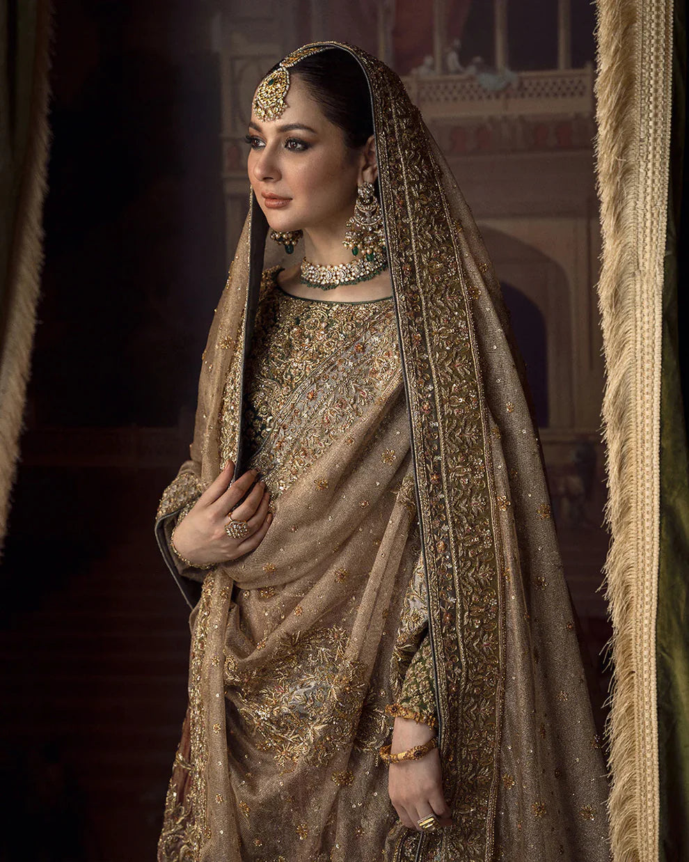 Faiza Saqlain Muntaha luxury bridal couture outfit front view featuring heavily hand-embellished raw silk shirt with intricate resham, dabka, naqshi and sequin embroidery in Mughal inspired floral motifs, paired with voluminous lehenga adorned with multiple richly embroidered borders and antique finishing, completed with a gracefully draped zari net dupatta with detailed adda work and ornate edging, premium bridal ensemble perfect for weddings, nikkah ceremonies and luxury festive occasions