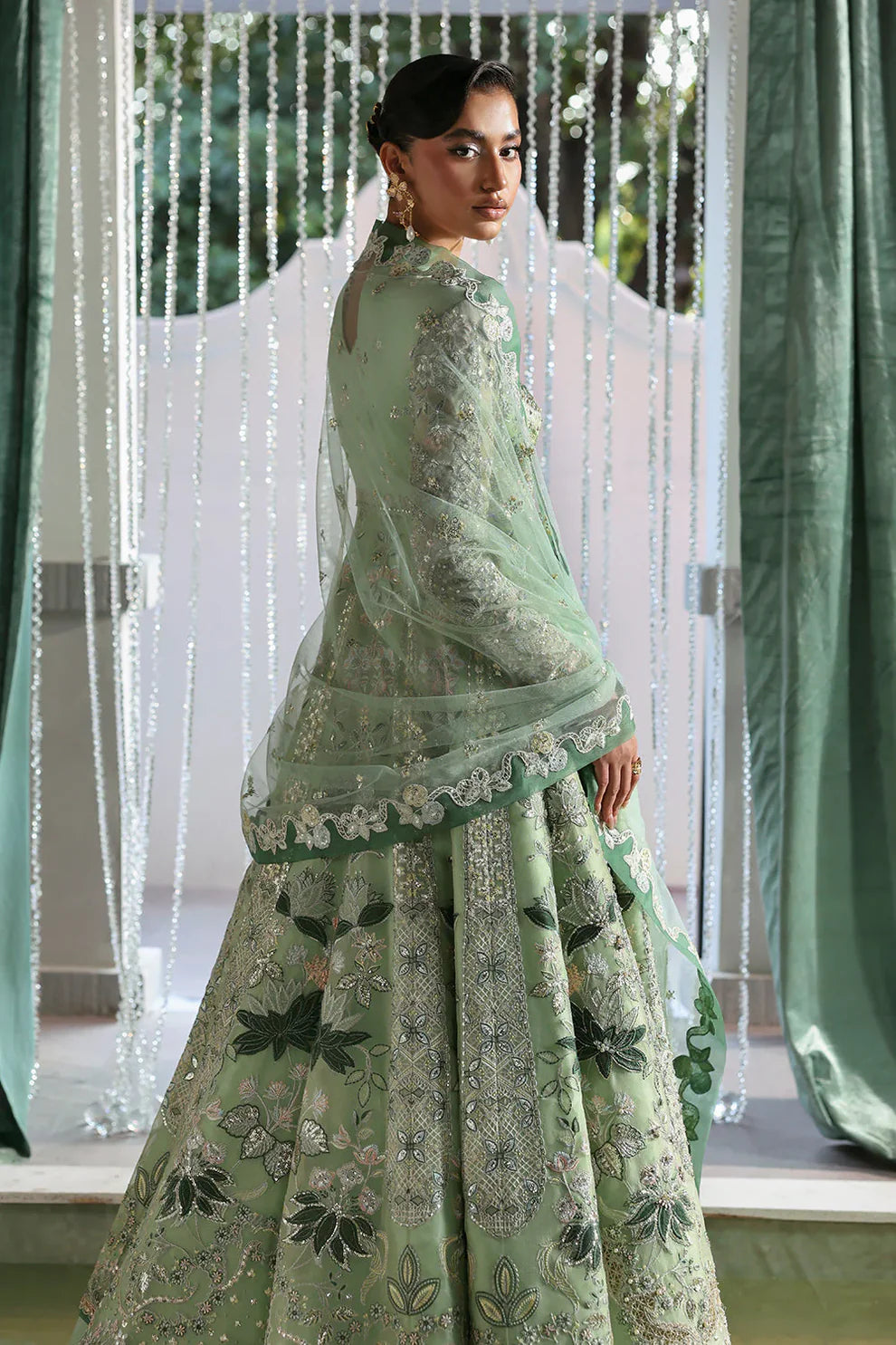 Lirien by Soraya luxury mint green couture pishwas outfit front view featuring heavily hand-embellished organza panels with intricate floral embroidery, resham threadwork, sequins, cutdana and tilla detailing arranged in elegant flowing pattern across flare, velvet accent neckline patch adding rich contrast, full embroidered sleeves and back panels, paired with lightweight net dupatta featuring embroidered sprays and delicate border finishing, along with dyed silk trouser, premium Pakistani designer outfit 