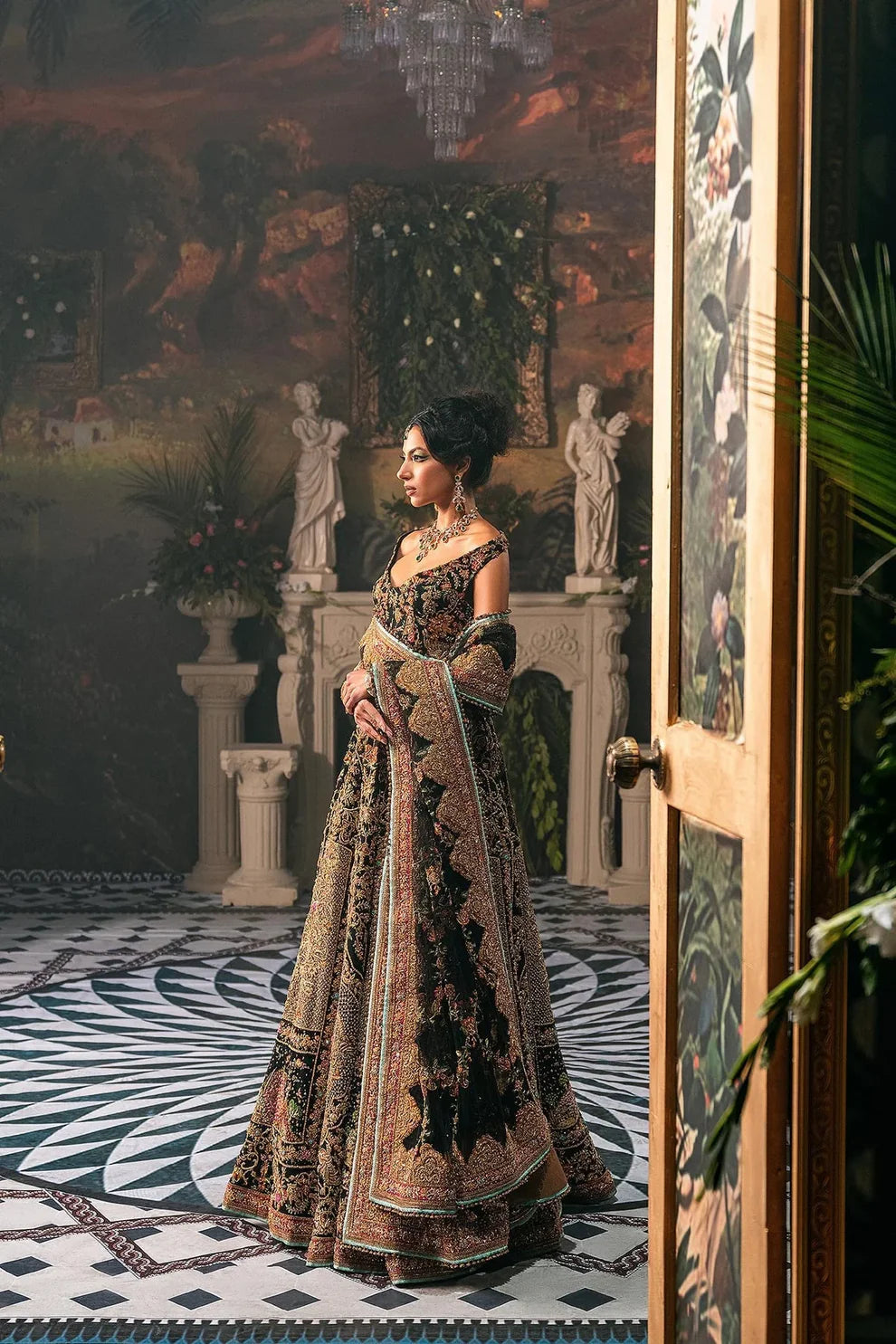 Ajooba by Fahad Hussayn luxury black bridal couture outfit front view featuring heavily hand-embellished net lehenga and blouse with intricate resham, zardozi, naqshi, dabka and crystal embroidery forming rich floral Mughal inspired patterns, dramatic structured silhouette with full flare lehenga and detailed choli, paired with sheer organza dupatta scattered with delicate floral motifs and ornate embroidered border finishing, premium high-end bridal ensemble perfect for weddings, receptions etc