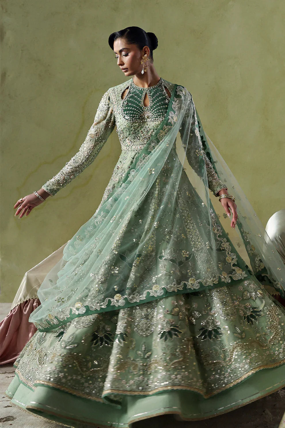 Lirien by Soraya luxury mint green couture pishwas outfit front view featuring heavily hand-embellished organza panels with intricate floral embroidery, resham threadwork, sequins, cutdana and tilla detailing arranged in elegant flowing pattern across flare, velvet accent neckline patch adding rich contrast, full embroidered sleeves and back panels, paired with lightweight net dupatta featuring embroidered sprays and delicate border finishing, along with dyed silk trouser, premium Pakistani designer outfit 