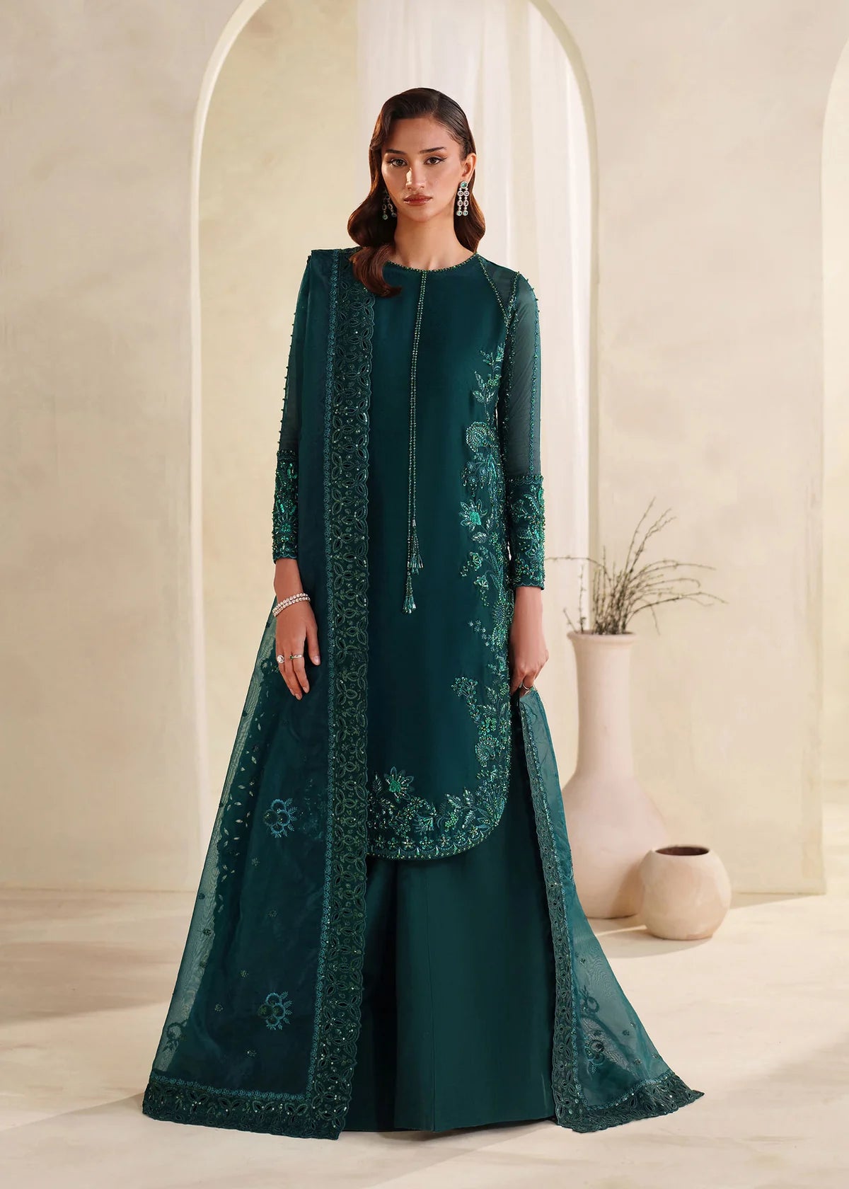 Eiza Dastoor luxury formal outfit front view featuring elegant ivory white raw silk shirt with heavy hand embroidery including intricate floral motifs, resham, sequins, kora and dabka embellishments arranged in refined symmetrical pattern, delicately detailed neckline and sleeve borders with fine craftsmanship, paired with matching straight trousers and soft organza dupatta with embroidered edges and light sequin spray, premium Pakistani designer outfit perfect for weddings, engagements, festive occasions 