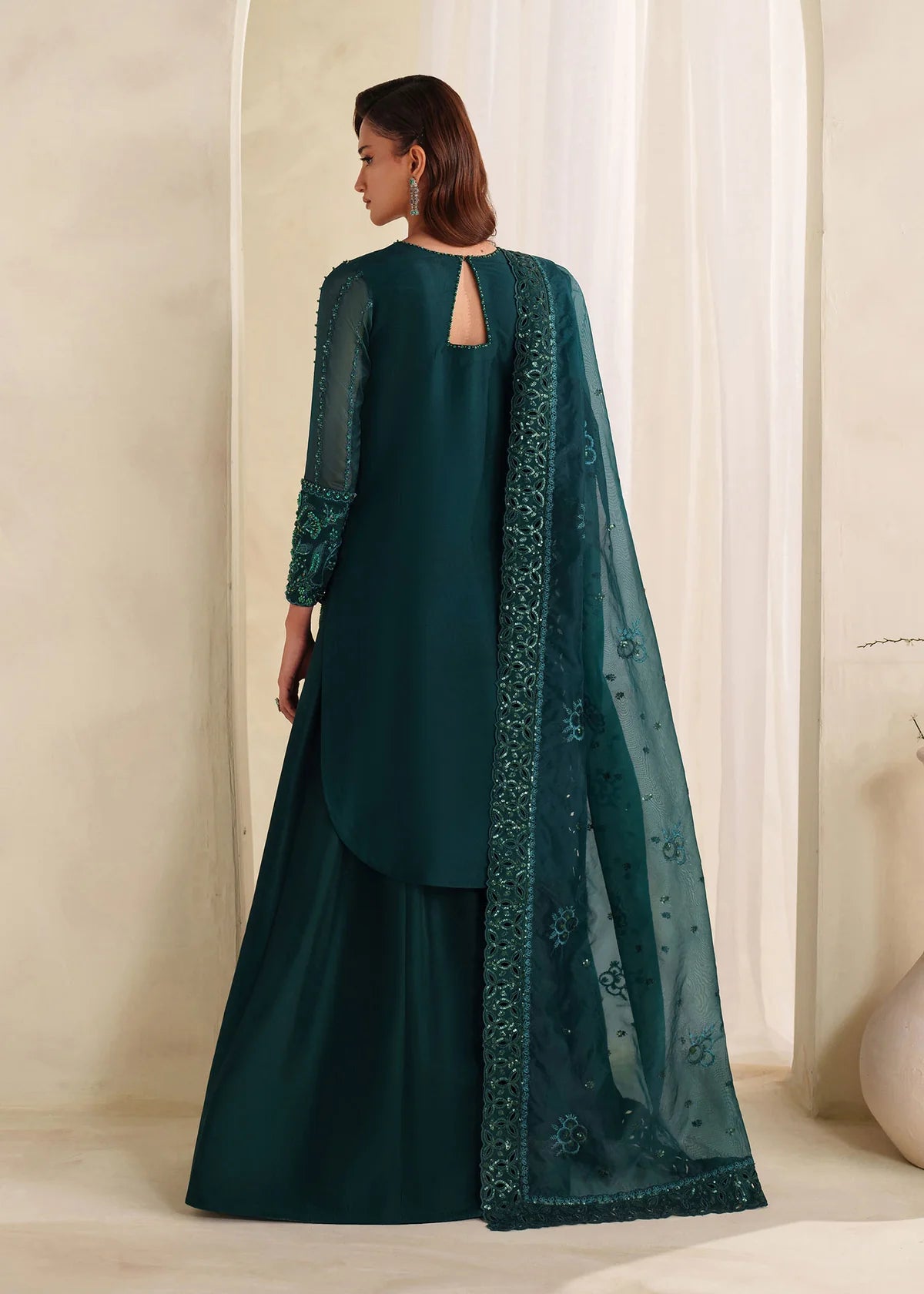 Eiza Dastoor luxury formal outfit front view featuring elegant ivory white raw silk shirt with heavy hand embroidery including intricate floral motifs, resham, sequins, kora and dabka embellishments arranged in refined symmetrical pattern, delicately detailed neckline and sleeve borders with fine craftsmanship, paired with matching straight trousers and soft organza dupatta with embroidered edges and light sequin spray, premium Pakistani designer outfit perfect for weddings, engagements, festive occasions 