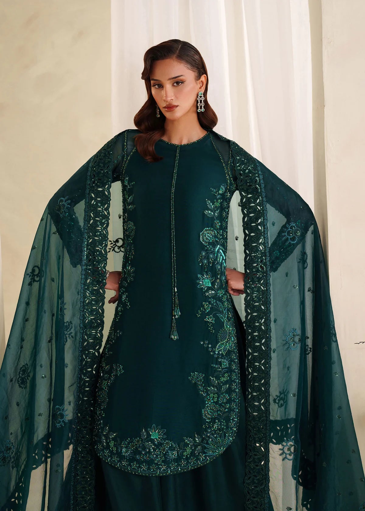 Eiza Dastoor luxury formal outfit front view featuring elegant ivory white raw silk shirt with heavy hand embroidery including intricate floral motifs, resham, sequins, kora and dabka embellishments arranged in refined symmetrical pattern, delicately detailed neckline and sleeve borders with fine craftsmanship, paired with matching straight trousers and soft organza dupatta with embroidered edges and light sequin spray, premium Pakistani designer outfit perfect for weddings, engagements, festive occasions 