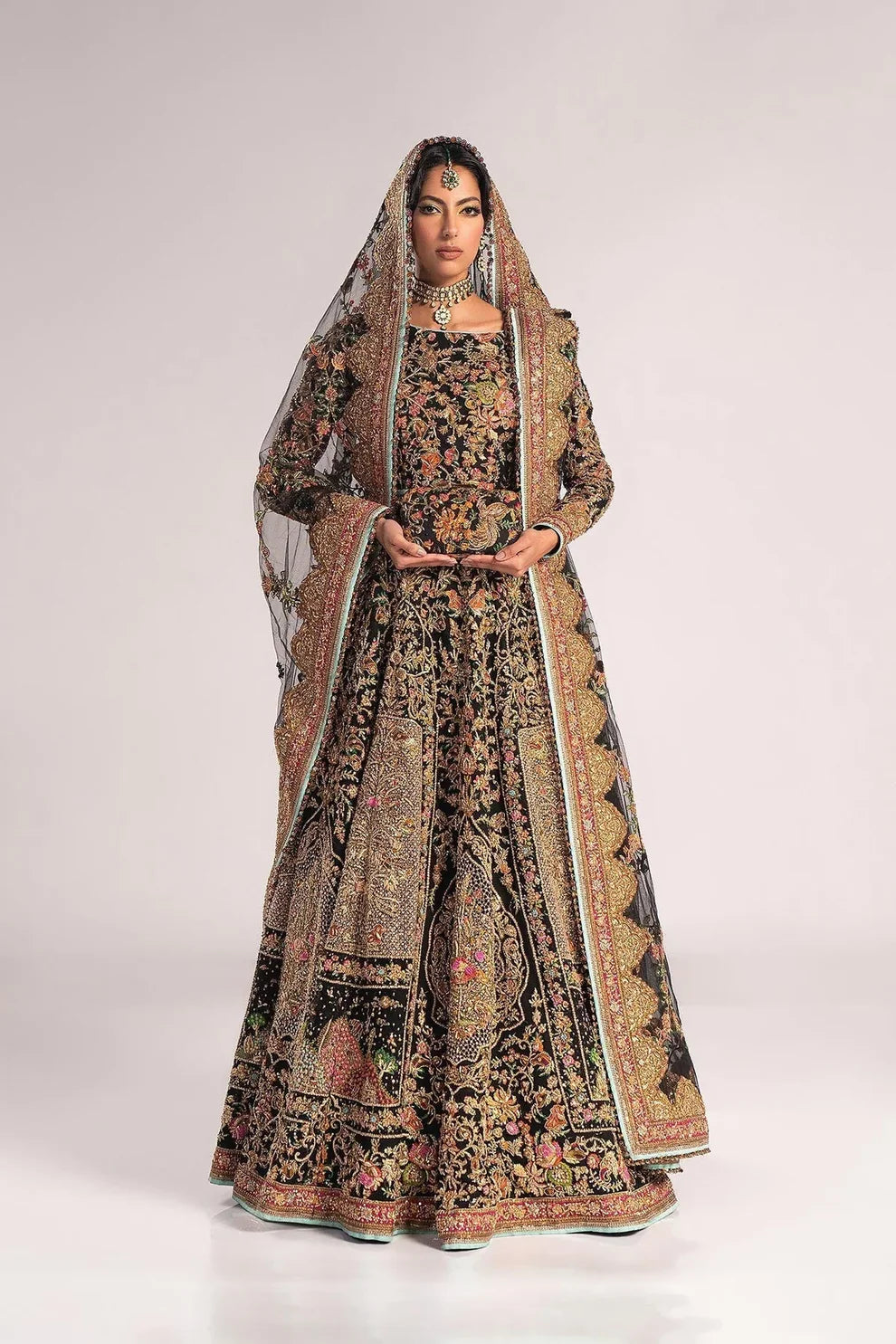 Ajooba by Fahad Hussayn luxury black bridal couture outfit front view featuring heavily hand-embellished net lehenga and blouse with intricate resham, zardozi, naqshi, dabka and crystal embroidery forming rich floral Mughal inspired patterns, dramatic structured silhouette with full flare lehenga and detailed choli, paired with sheer organza dupatta scattered with delicate floral motifs and ornate embroidered border finishing, premium high-end bridal ensemble perfect for weddings, receptions etc