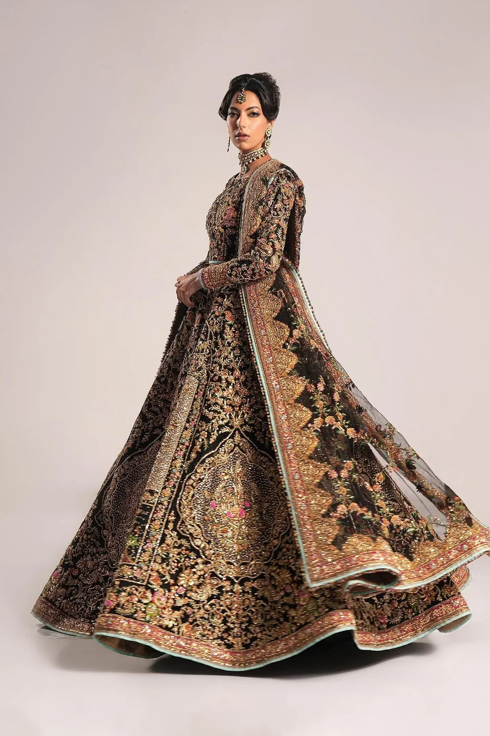Ajooba by Fahad Hussayn luxury black bridal couture outfit front view featuring heavily hand-embellished net lehenga and blouse with intricate resham, zardozi, naqshi, dabka and crystal embroidery forming rich floral Mughal inspired patterns, dramatic structured silhouette with full flare lehenga and detailed choli, paired with sheer organza dupatta scattered with delicate floral motifs and ornate embroidered border finishing, premium high-end bridal ensemble perfect for weddings, receptions etc