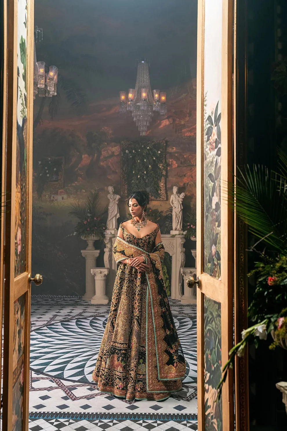 Ajooba by Fahad Hussayn luxury black bridal couture outfit front view featuring heavily hand-embellished net lehenga and blouse with intricate resham, zardozi, naqshi, dabka and crystal embroidery forming rich floral Mughal inspired patterns, dramatic structured silhouette with full flare lehenga and detailed choli, paired with sheer organza dupatta scattered with delicate floral motifs and ornate embroidered border finishing, premium high-end bridal ensemble perfect for weddings, receptions etc