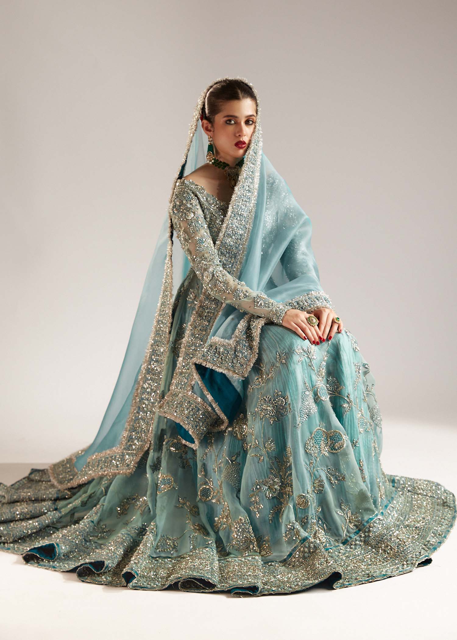 Full view of Astra ice blue embellished peshwas sharara with model sitting on stool in elegant pose