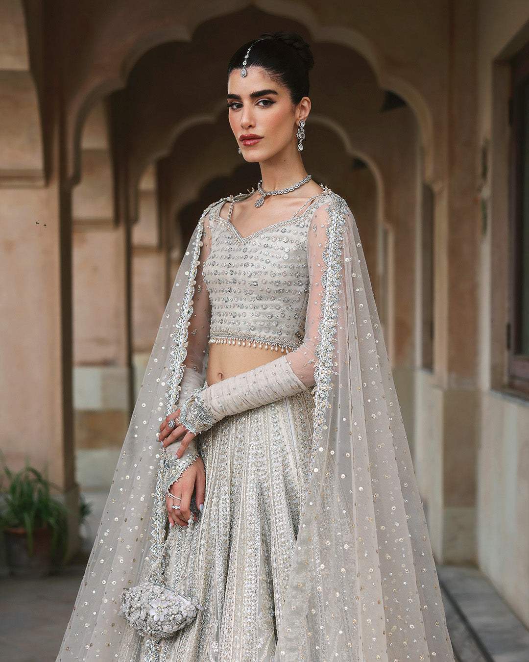 Left side full view of model wearing Faiza Saqlain Cammi white embellished bridal lehenga choli with net dupatta