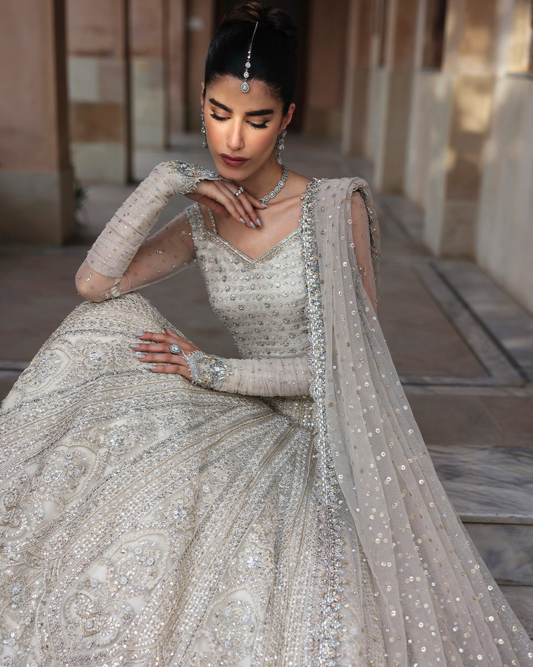 Model sitting on stairs wearing Faiza Saqlain Cammi white embellished bridal lehenga choli elegant pose
