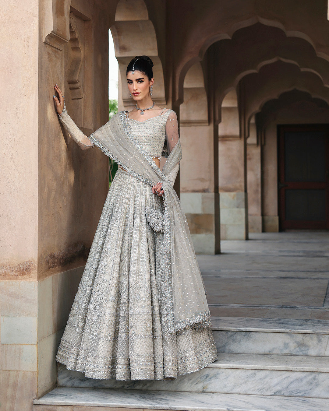 Full view of model wearing Faiza Saqlain Cammi white embellished bridal lehenga choli with net dupatta
