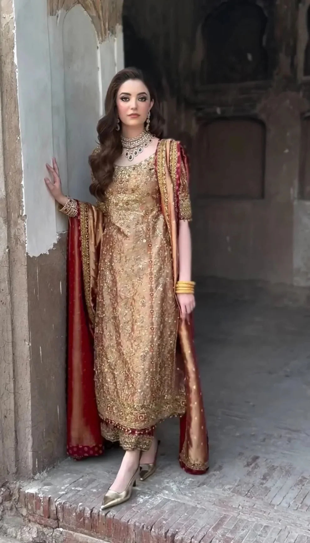 Meerub by Haris Shakeel luxury formal outfit front view featuring deep bronze raw silk shirt with intricate all-over gold hand embroidery, delicate floral motifs, zari and resham threadwork with refined sequin accents, elegantly structured straight silhouette with richly embellished neckline and sleeve borders, paired with matching straight trousers and beautifully coordinated dupatta with embroidered pallu and subtle maroon piping, premium Pakistani designer outfit perfect for weddings.