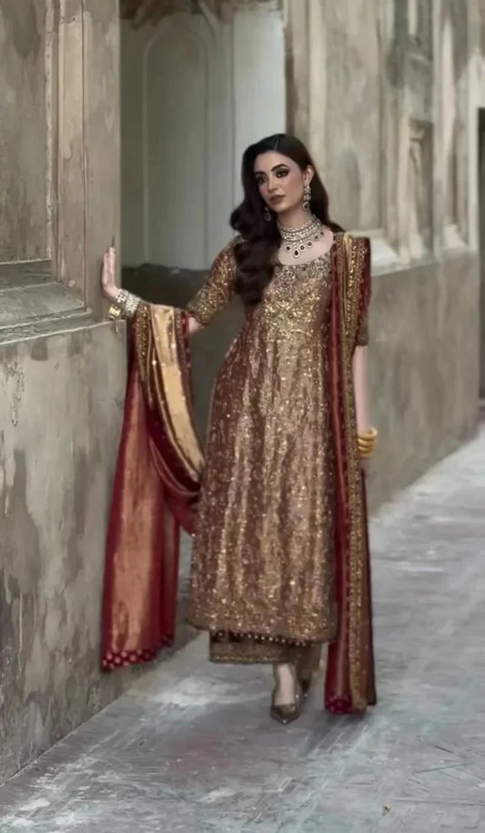 Meerub by Haris Shakeel luxury formal outfit front view featuring deep bronze raw silk shirt with intricate all-over gold hand embroidery, delicate floral motifs, zari and resham threadwork with refined sequin accents, elegantly structured straight silhouette with richly embellished neckline and sleeve borders, paired with matching straight trousers and beautifully coordinated dupatta with embroidered pallu and subtle maroon piping, premium Pakistani designer outfit perfect for weddings, mehndi, baraat etc