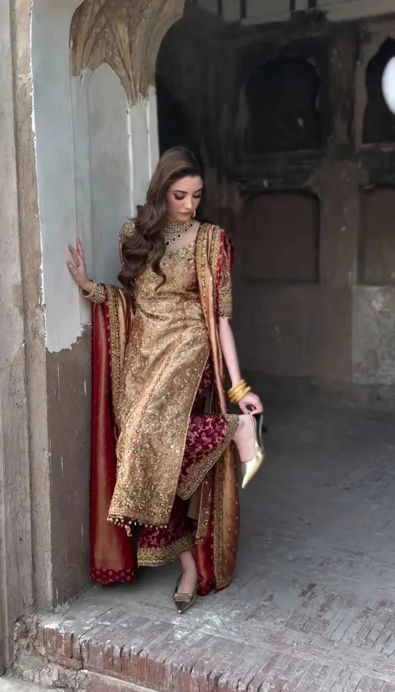 Meerub by Haris Shakeel luxury formal outfit front view featuring deep bronze raw silk shirt with intricate all-over gold hand embroidery, delicate floral motifs, zari and resham threadwork with refined sequin accents, elegantly structured straight silhouette with richly embellished neckline and sleeve borders, paired with matching straight trousers and beautifully coordinated dupatta with embroidered pallu and subtle maroon piping, premium Pakistani designer outfit perfect for weddings, mehndi, baraat