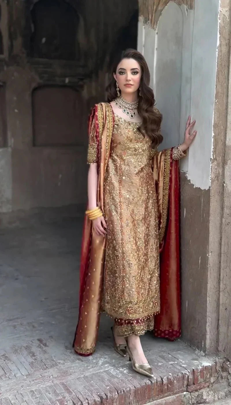 Meerub by Haris Shakeel luxury formal outfit front view featuring deep bronze raw silk shirt with intricate all-over gold hand embroidery, delicate floral motifs, zari and resham threadwork with refined sequin accents, elegantly structured straight silhouette with richly embellished neckline and sleeve borders, paired with matching straight trousers and beautifully coordinated dupatta with embroidered pallu and subtle maroon piping, premium Pakistani designer outfit perfect for weddings, mehndi, baraat 