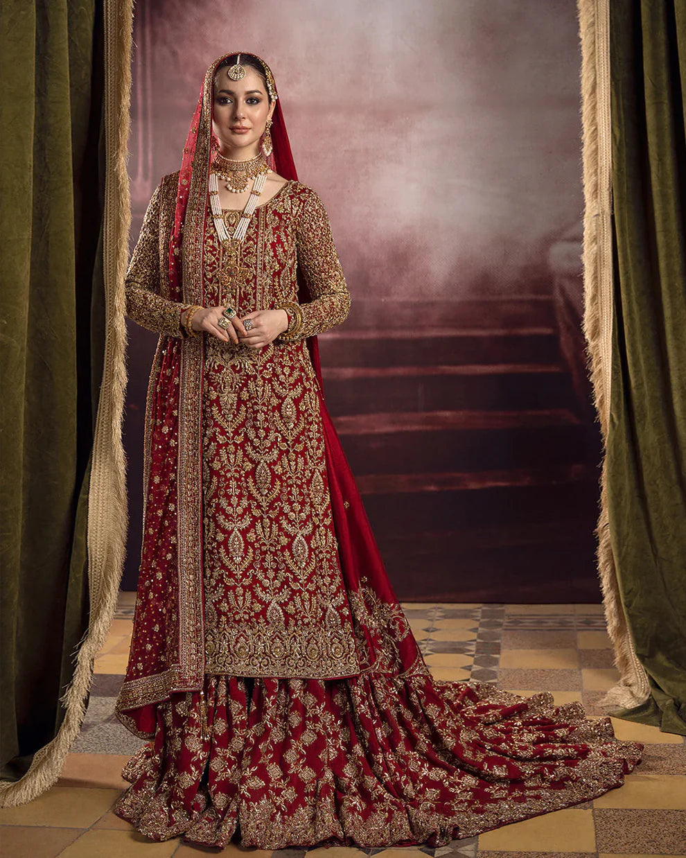 Roushana Faiza Saqlain luxury red bridal couture outfit front view featuring heavily hand-embellished chiffon pishwas with intricate dabka, marori, resham and zardozi embroidery forming traditional floral and vine motifs, richly detailed neckline and sleeves with full handwork, paired with Korean raw silk gharara with fine embellishment and flowing net dupatta adorned with heavy embroidery and ornate border finishing, premium bridal wedding dress perfect for brides, receptions and luxury festive occasions.